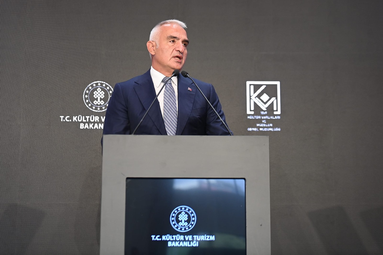 Kürsüde konuşan yetkilinin bakanlık logolu fon önündeki yakın plan görüntüsü