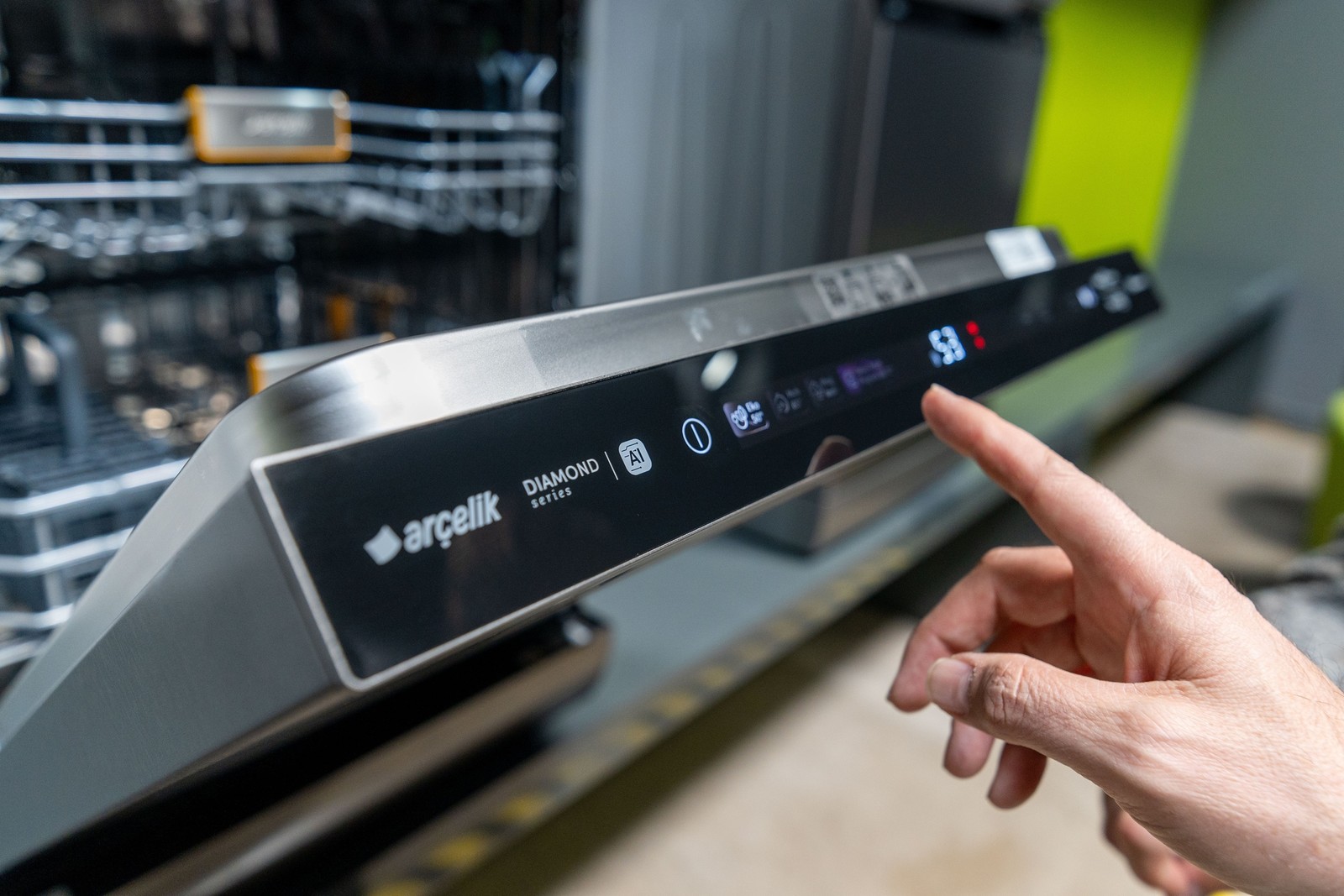 Arçelik Diamond Series bulaşık makinesinin kontrol panelinde eko ayarına uzanan bir el; arka planda açık makine sepeti.