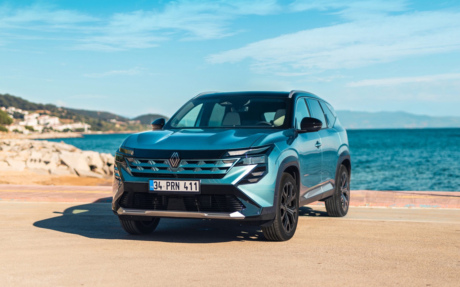 Deniz kıyısında beton zeminde duran mavi Renault SUV'nin önden tanıtım fotoğrafı